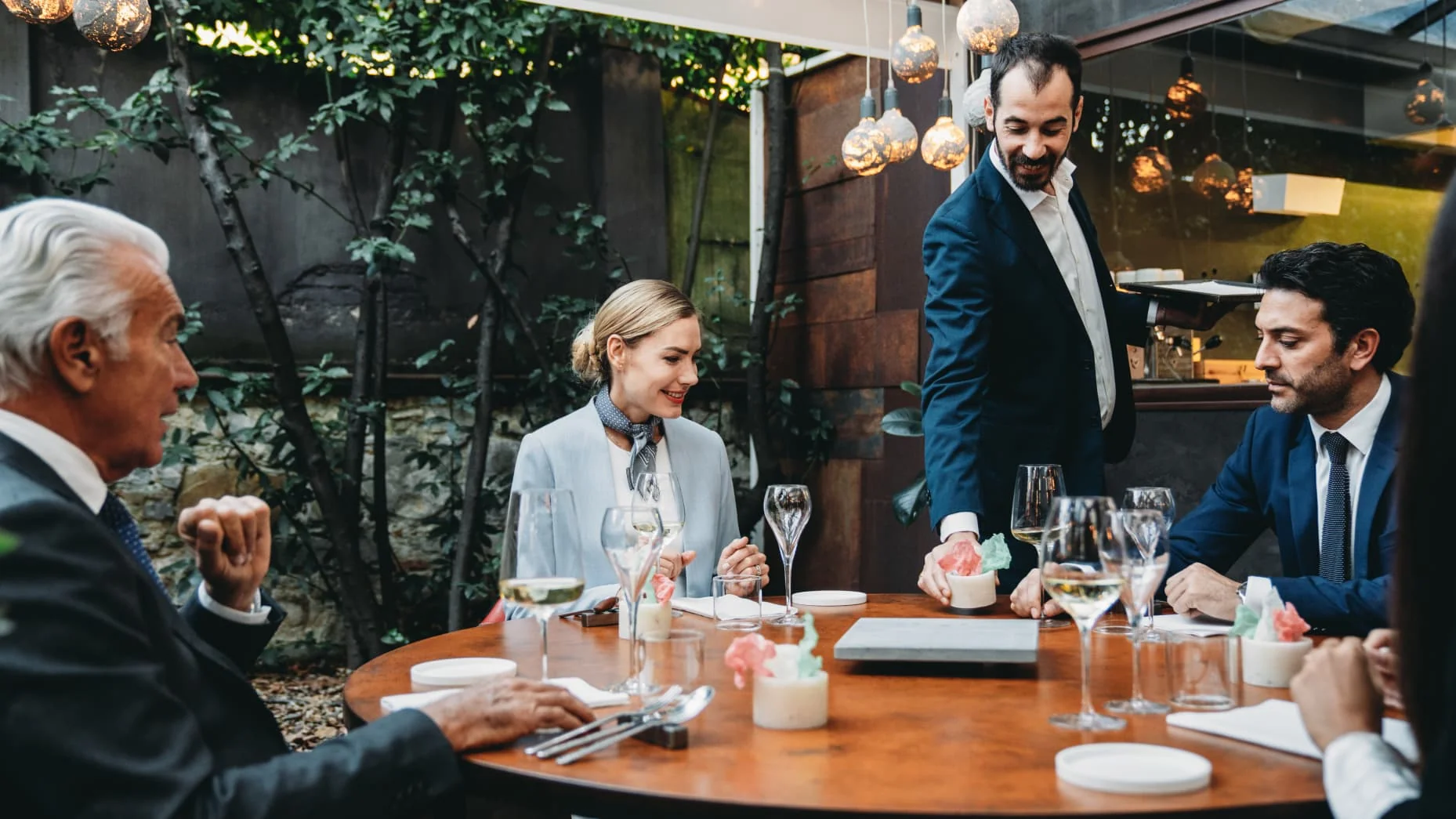 Colleagues are enjoying a meal at the restaurant during a meeting. Elegant high-end restaurant. A waiter is serving them.